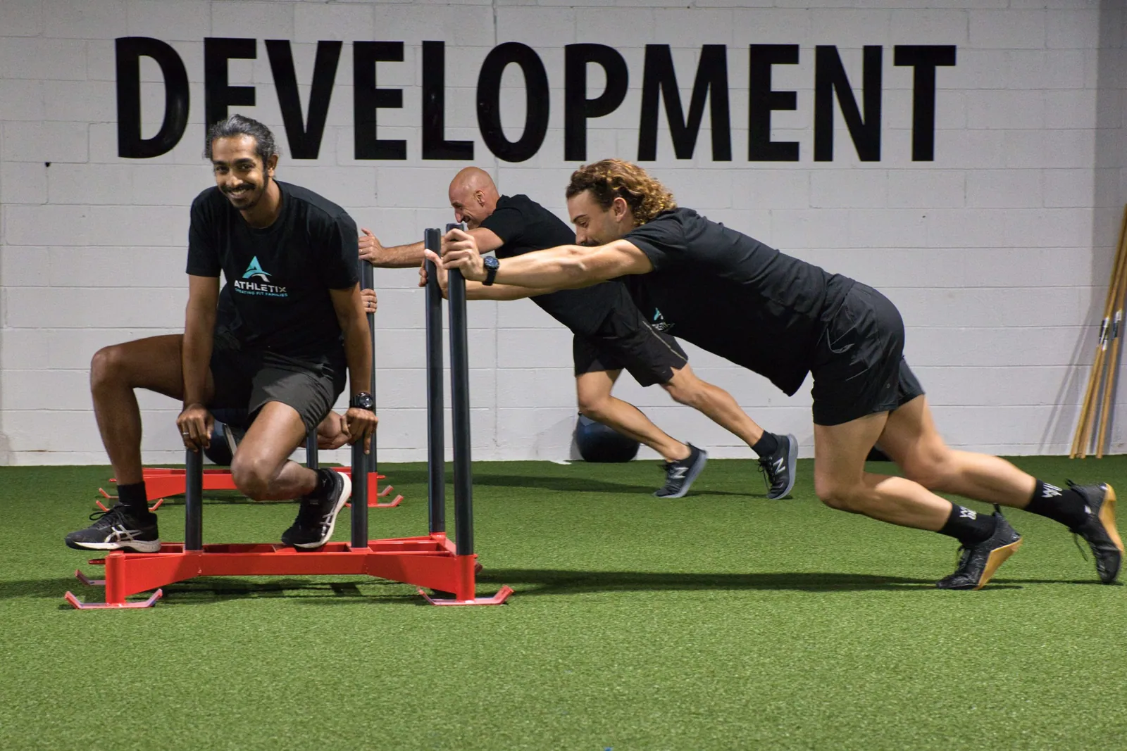Athletes sled pushing under the ATHLETIC DEVELOPMENT wall at ATHLETIX Brisbane